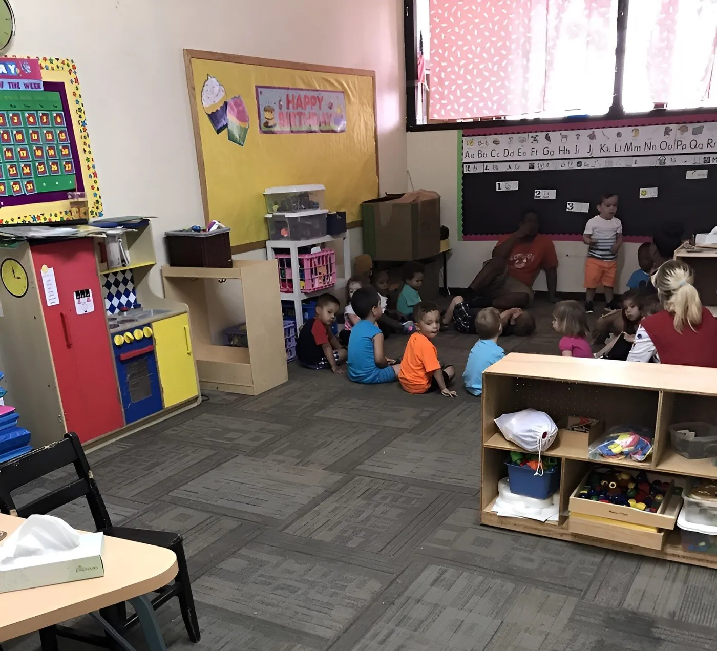 A bright classroom with children gathered on the rug