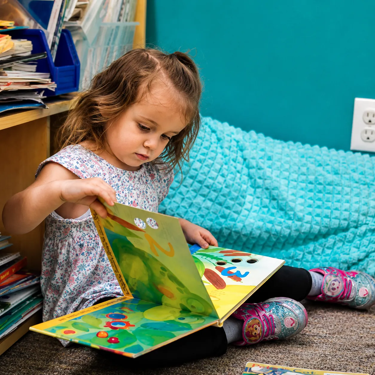 A little girl reading a picture book on the classroom floor