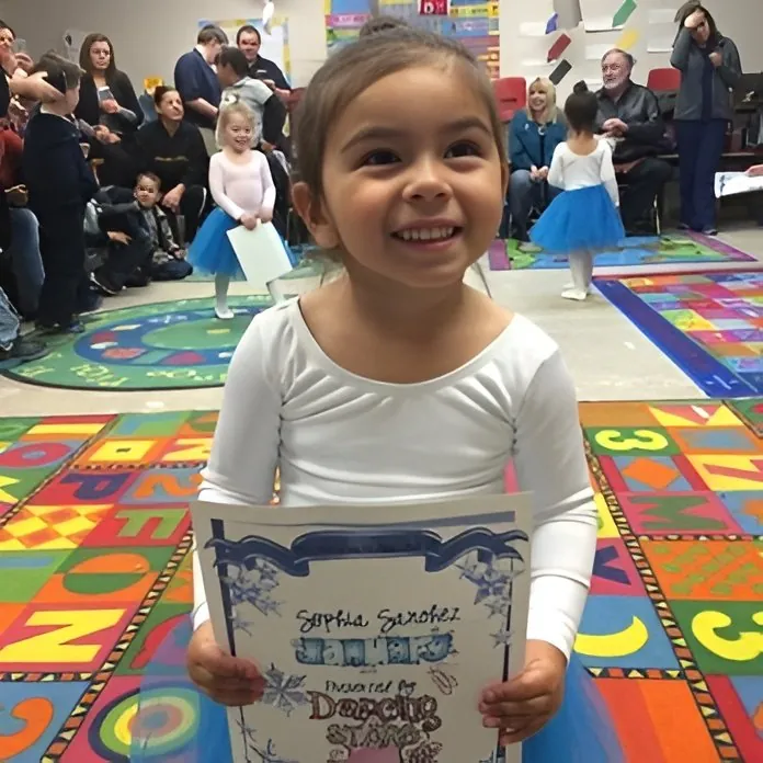 A smiling girl in a ballet outfit holding her recital certificate