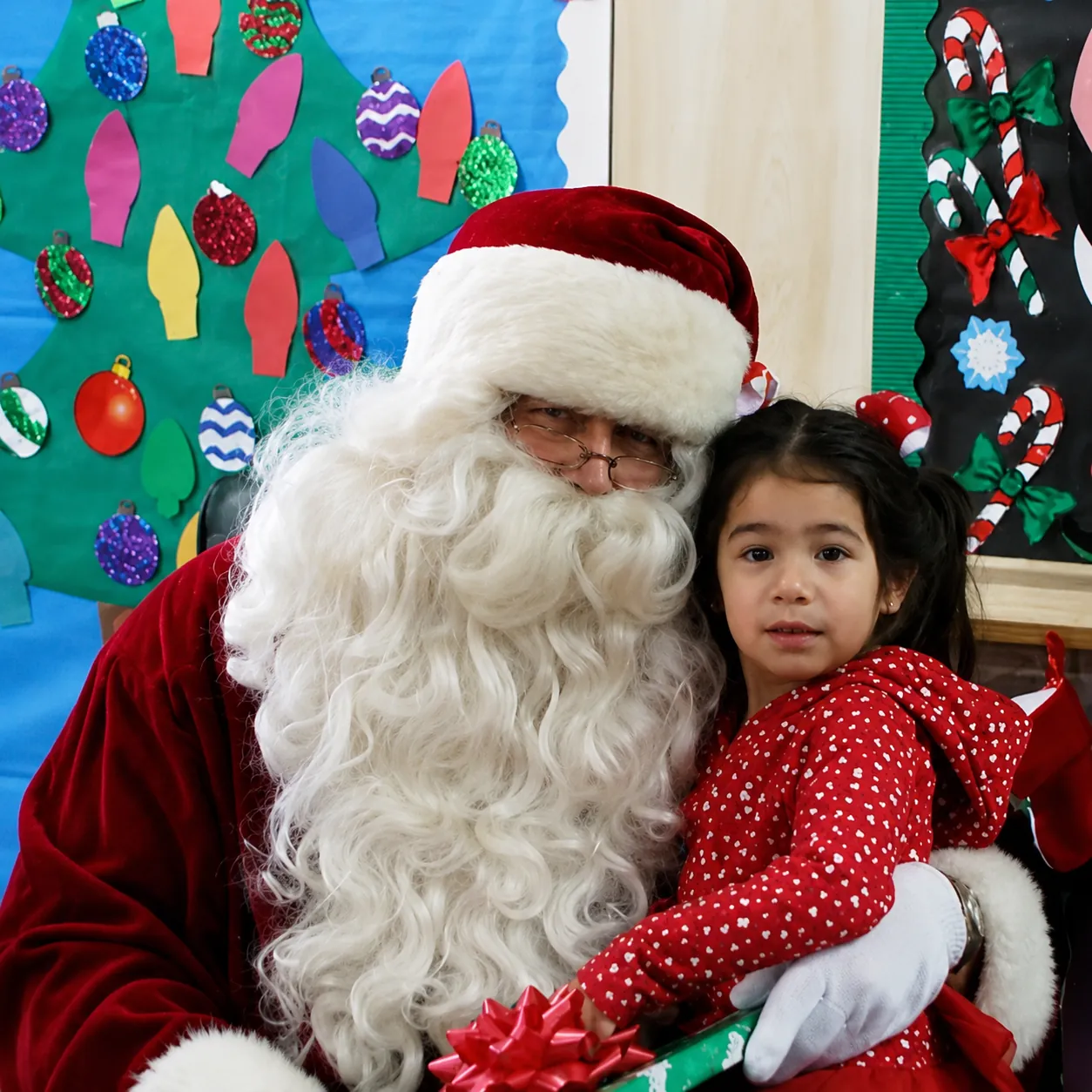 A little girl in a red dress sitting with Santa at the Castle